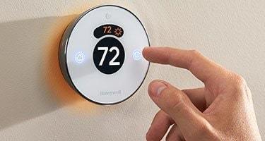 A hand adjusting a white smart thermostat dial