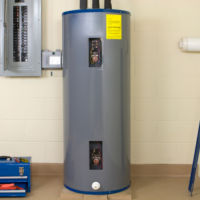 Gray tank water heater next to a breaker box and blue tool box