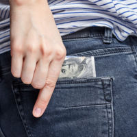 Woman Puts Money In Her Back Pocket Of A Jeans