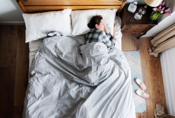 Clothed woman sleeping in a bed with gray & white sheets