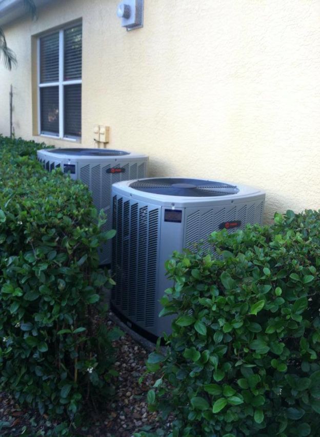 Two outdoor ground AC units surrounded by shrubbery