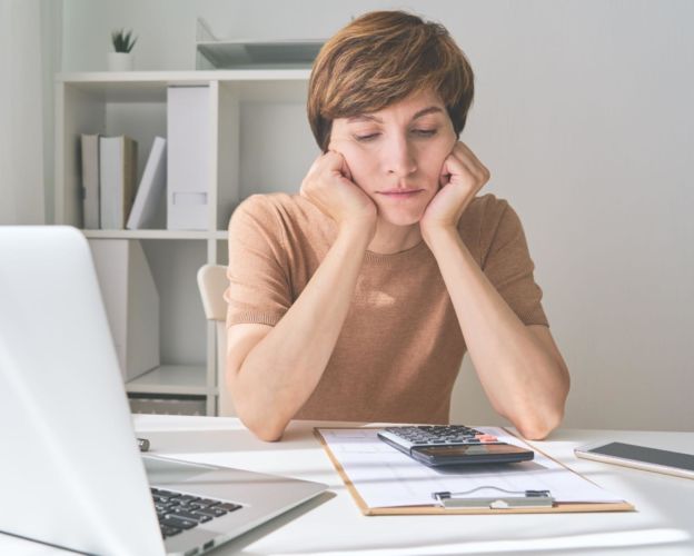 Frustrated woman resting face on hands looking at a calculator