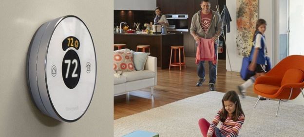 A touch screen smart thermostat on a white wall with a family.